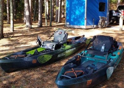 A set of sit-on kayaks set outside on the ground at a campsite with a CORE ICE trailer used for camping in the woods