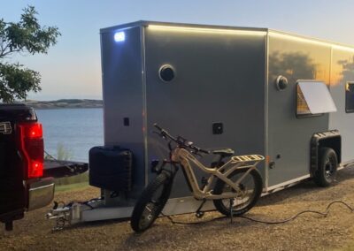 An off-road pedal bike sitting outside a CORE RV model in the night with the exterior LED lighting on and a window open