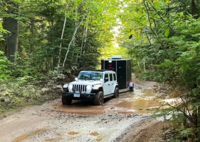 A Rubicon Jeep pulling a black CORE ICE trailer through the mud in the woods