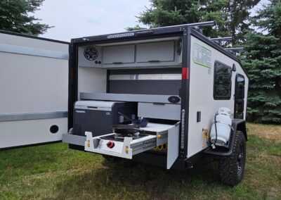 A view of the back galley of the CORE RV 5510 model. A fridge slide with a Dometic fridge, an LP pull-out cook-top with a cast iron atop and a bowl with spatula. An LP tank is mounted to the camp side behind the fender