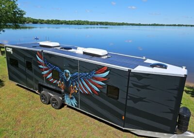 A top-view of a CORE RV 8032 model by the water with a roof of solar panels and a person in a kayak in the distance