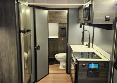 Interior view of CORE RV bathroom and kitchenette featuring a convection microwave, sink, cooktop and stove and large refrigerator